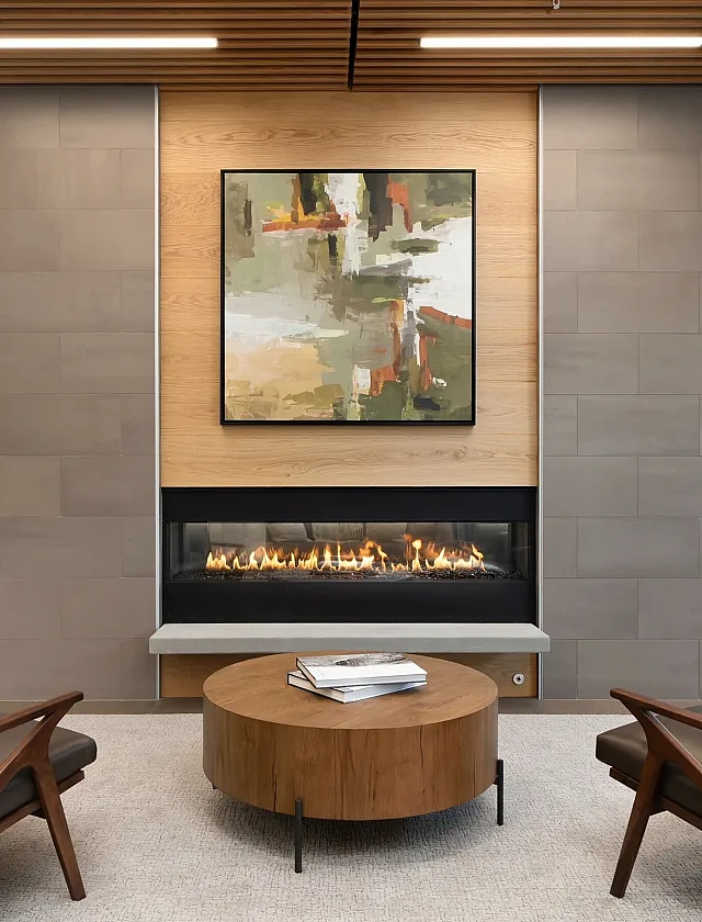 Elegant modern lounge area with leather armchairs, a central wooden table, and a cozy fireplace beneath abstract art.