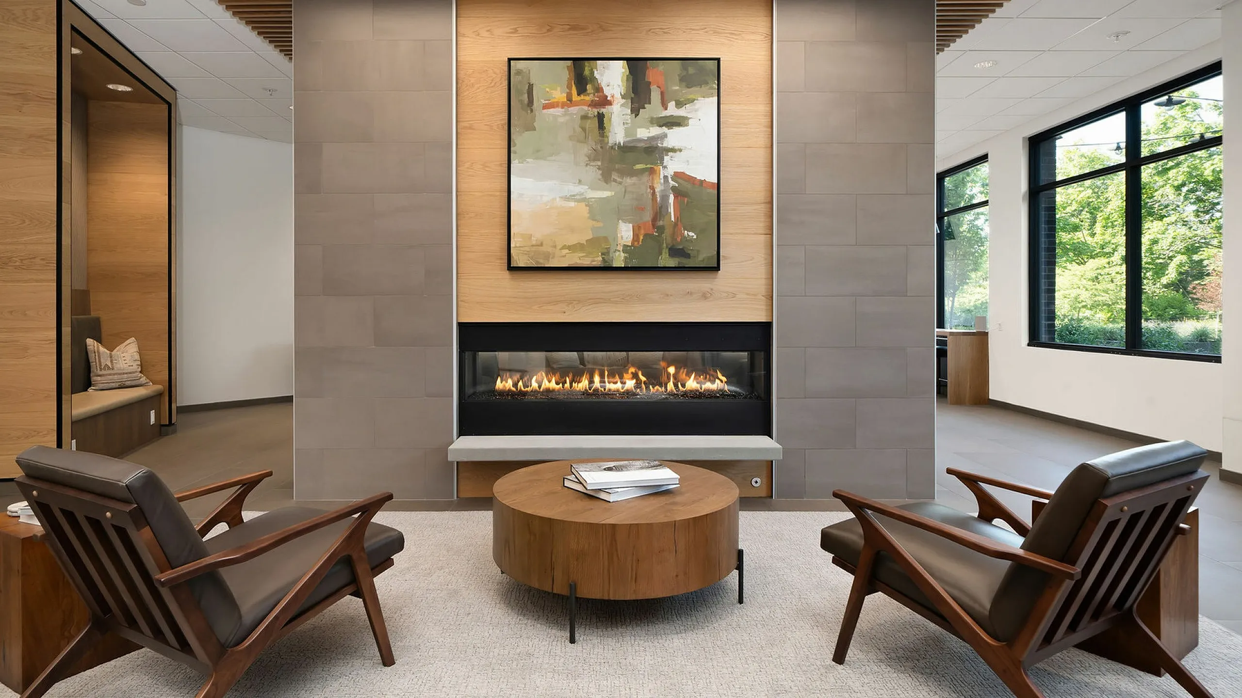 Chic modern lounge with elegant fireplace, stylish wooden chairs, abstract art, and large windows offering a serene view of greenery.