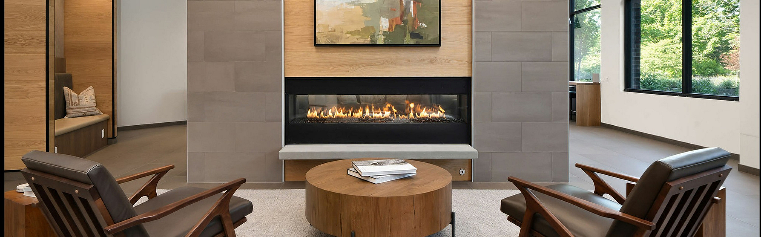 Modern living room with elegant fireplace, stylish armchairs, and large windows overlooking lush greenery.