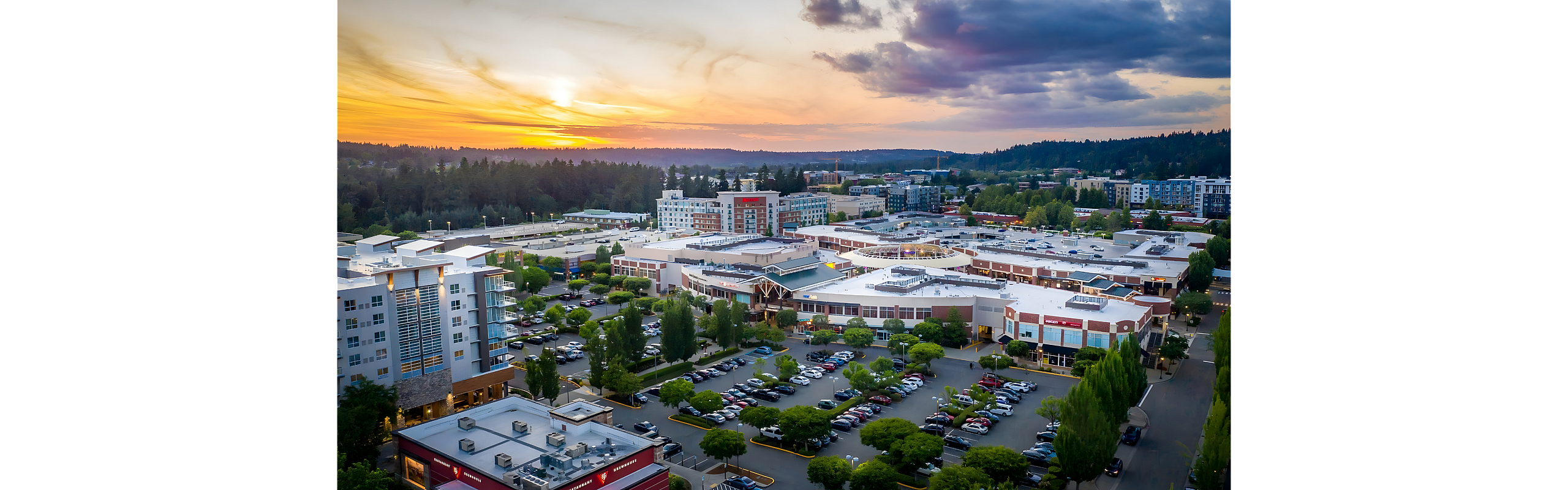 Stunning aerial view of a vibrant urban neighborhood at sunset, featuring modern buildings, lush greenery, and a spacious parking area.