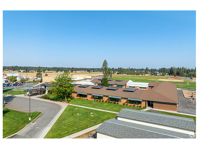Aerial view of a modern education campus featuring expansive green fields and a stylish brick building under a clear blue sky.