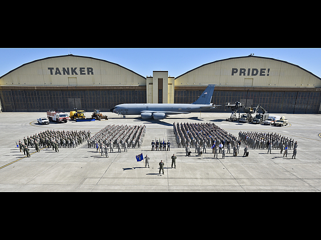 Impressive formation of uniformed personnel in front of a massive hangar labeled 'TANKER PRIDE', with a large military aircraft and various support vehicles in the background.