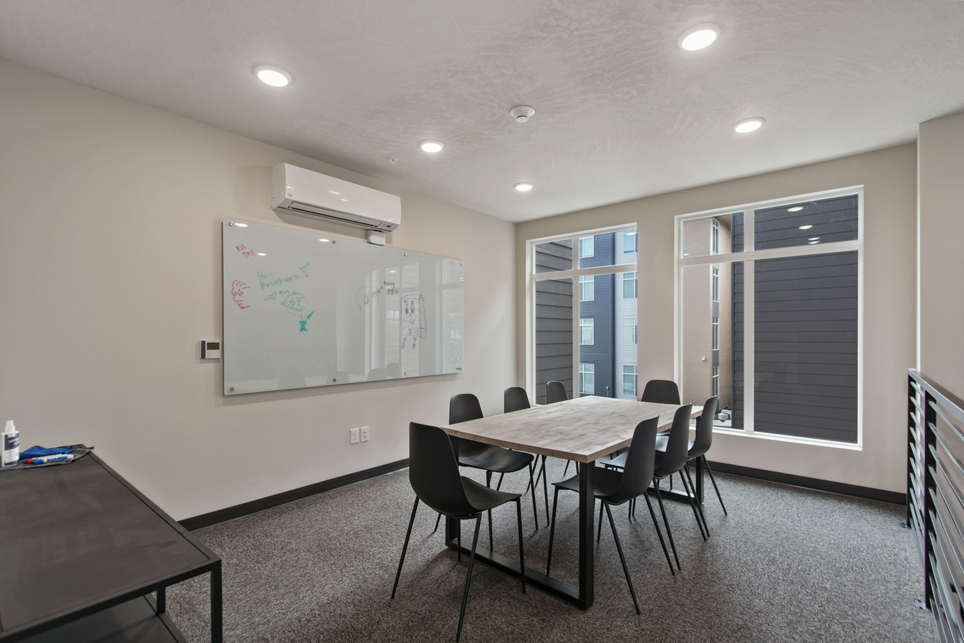 Modern meeting room with elegant table, black chairs, whiteboard, and large windows enhancing natural light.
