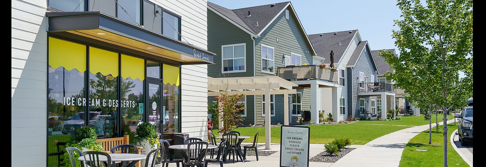 Charming neighborhood scene showcasing modern townhouses with a vibrant ice cream and desserts shop, inviting patios, and lush green surroundings.