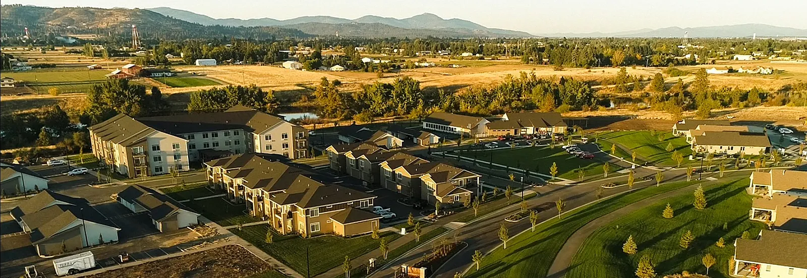 Aerial view of a picturesque residential community surrounded by lush greenery and scenic landscape, featuring modern apartment buildings and winding roads.
