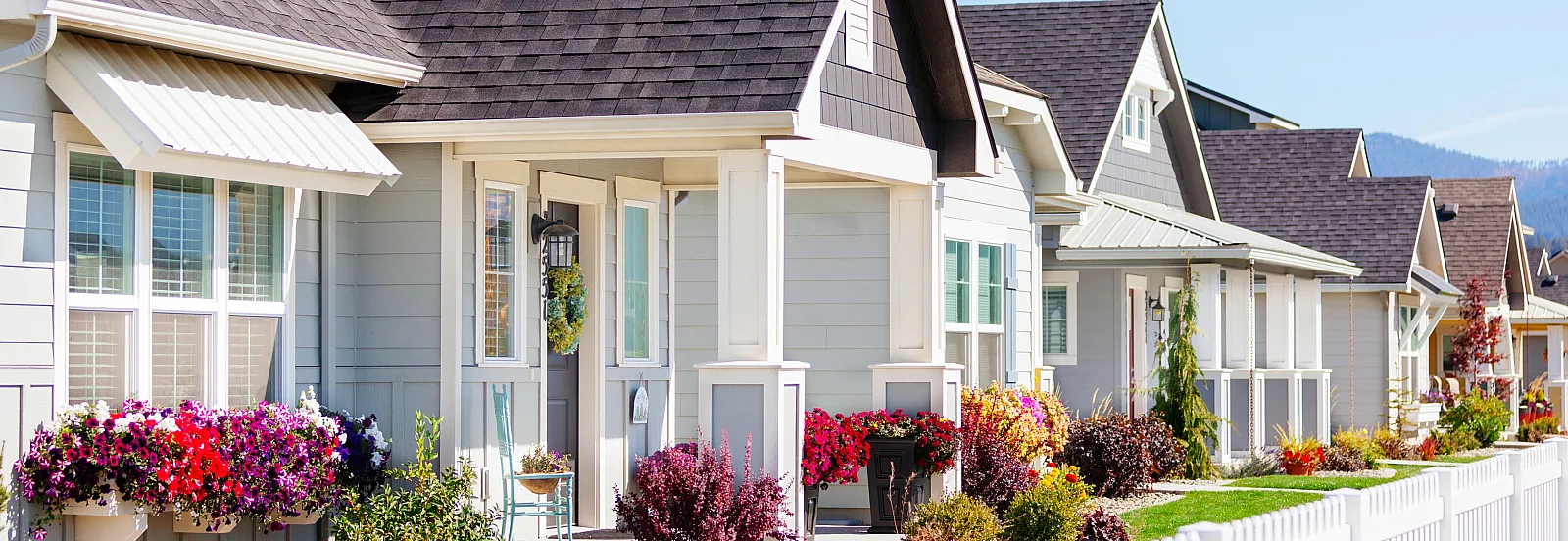 Charming suburban houses with vibrant flower beds and white picket fences, showcasing a picturesque neighborhood setting.