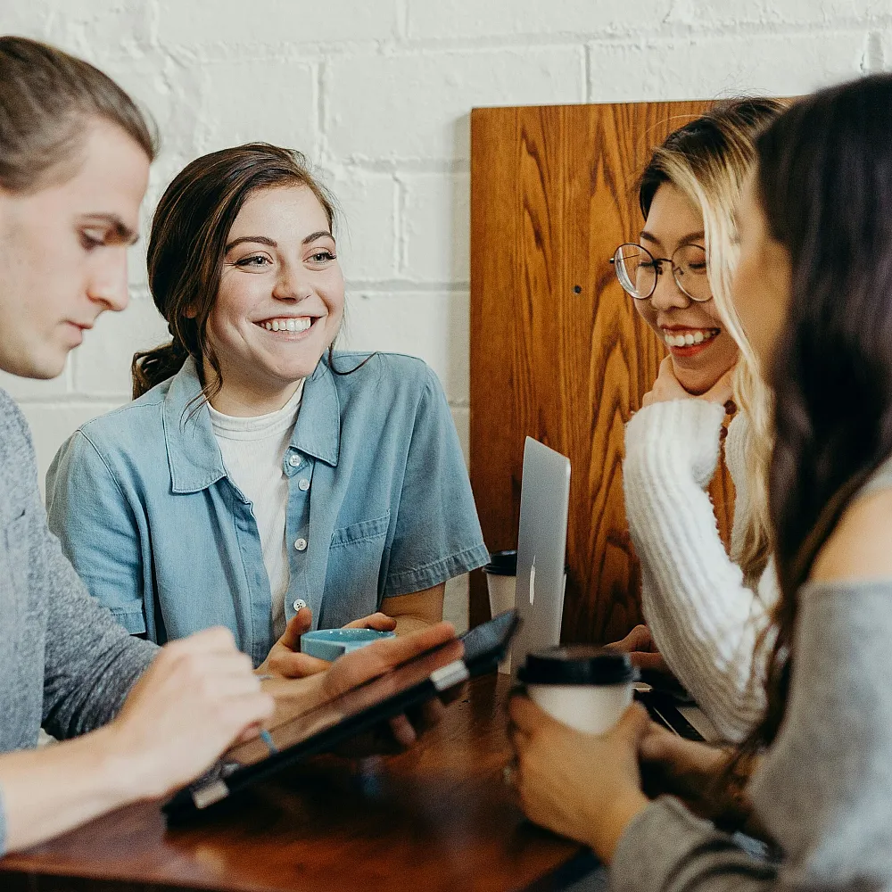 Lively group of young professionals collaborating over coffee and laptops in a cozy meeting space, exuding creativity and teamwork.