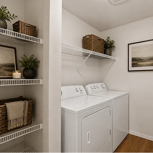 Charming laundry room featuring modern washer and dryer, elegant shelving with stylish decor, and warm wooden flooring.