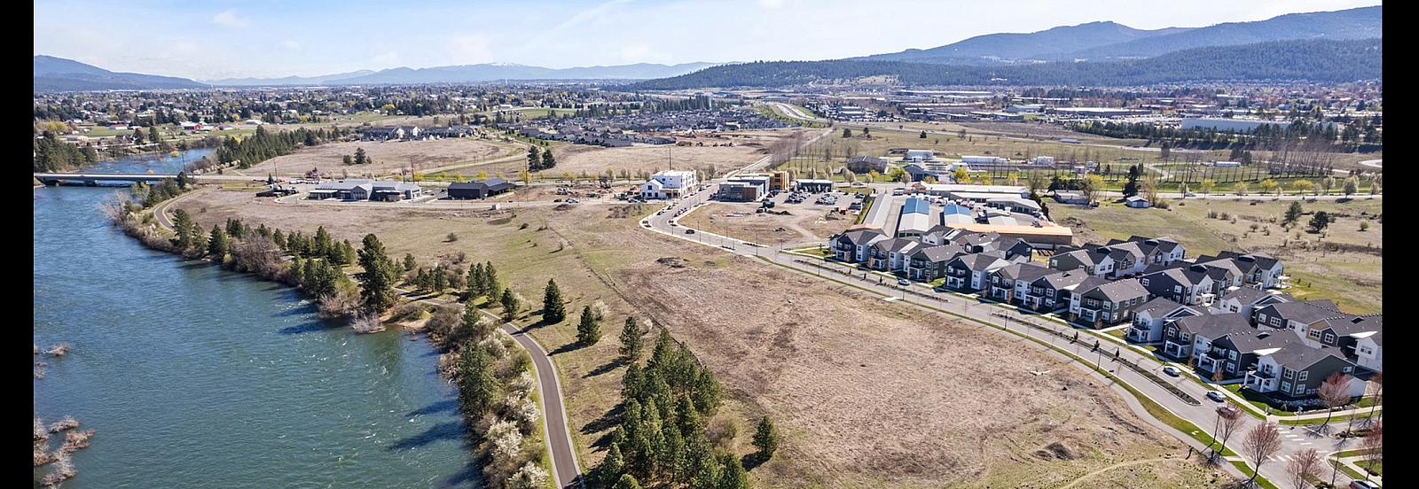 Scenic aerial view showcasing a riverside community with modern townhouses, lush greenery, and picturesque mountain backdrop.