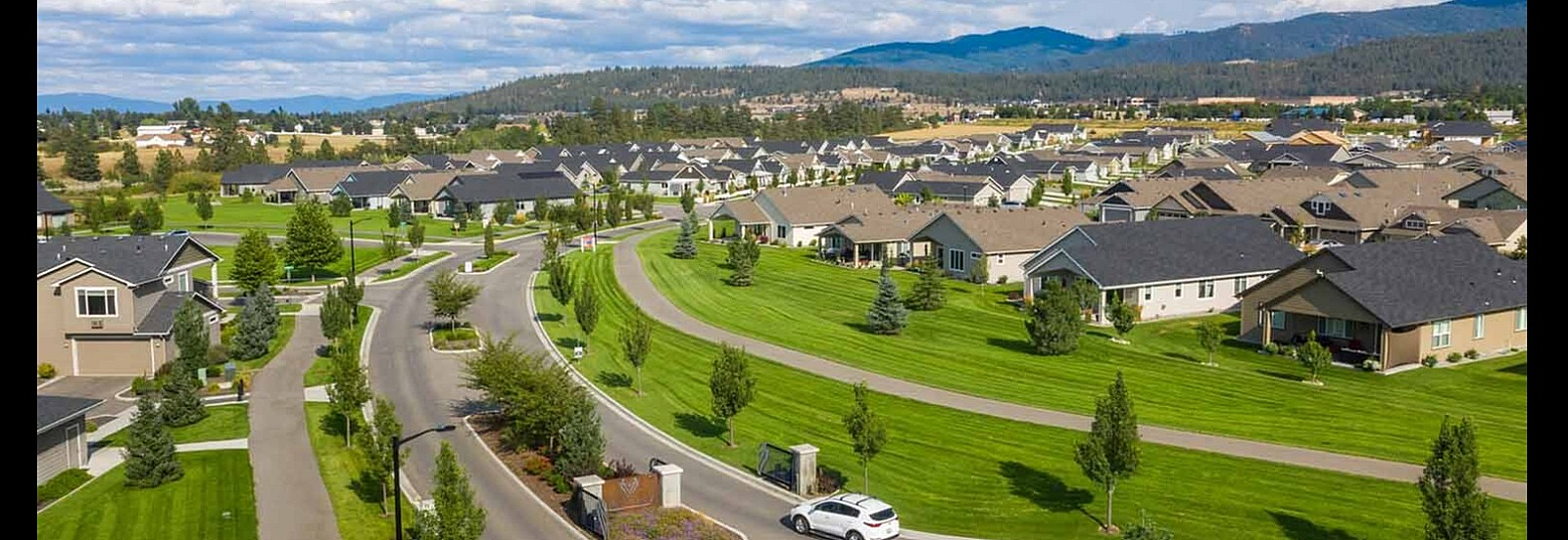 Aerial view of picturesque suburban neighborhood with charming houses, manicured lawns, and winding streets set against a backdrop of rolling hills.