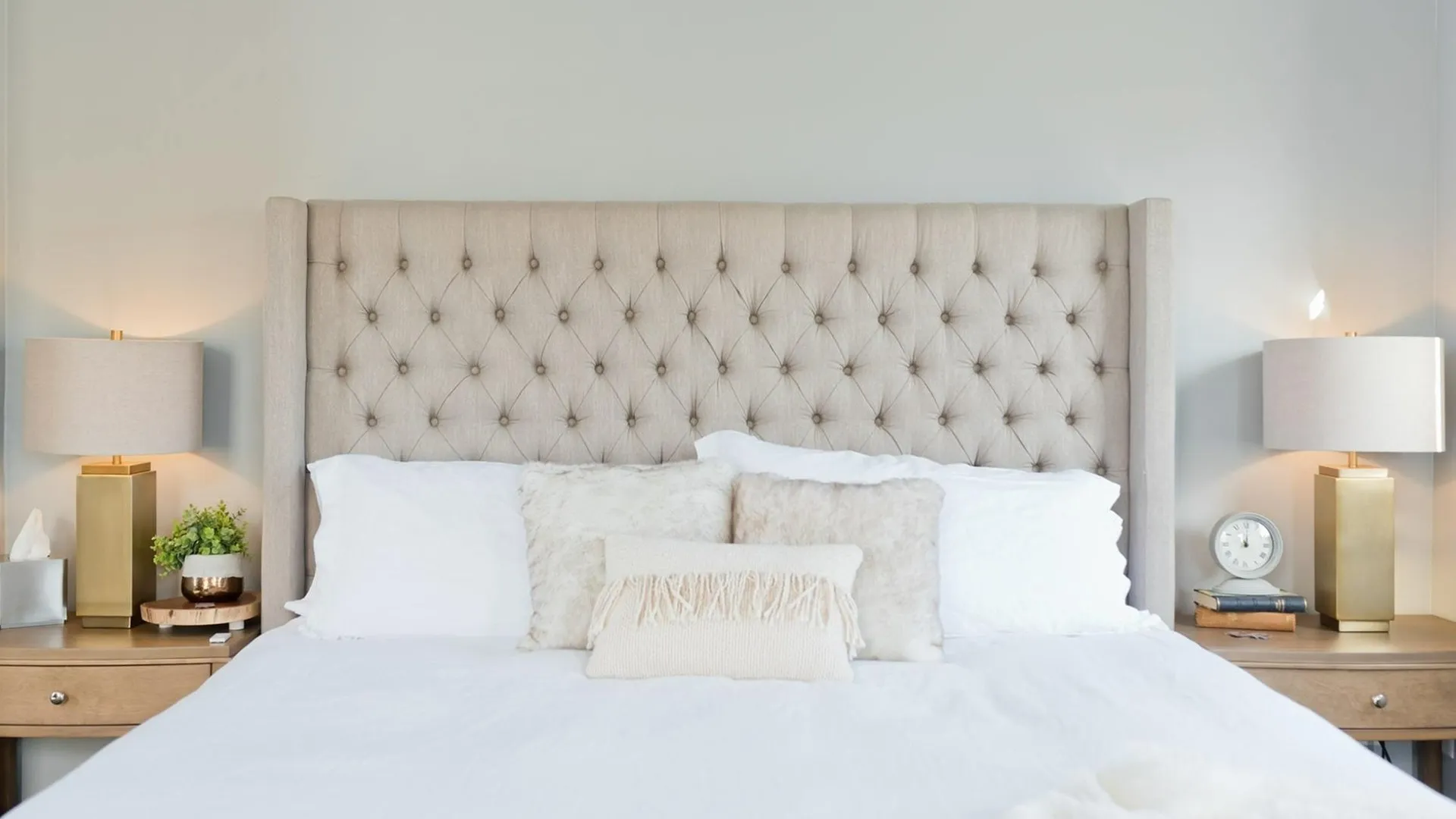 Queen bed with quilted headboard, cream colored bedding and side tables with lamps and books.