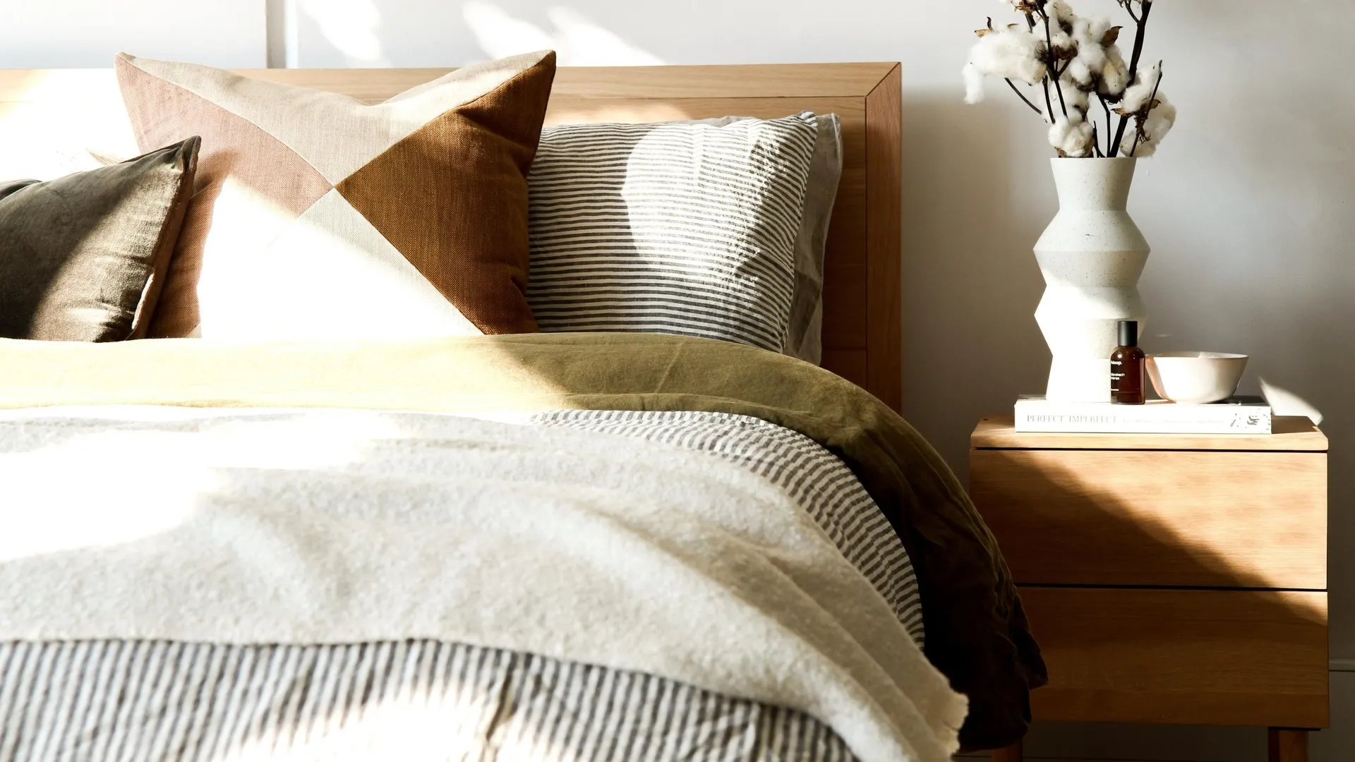 Bed partially visible with side table holding cotton in a vase and books.