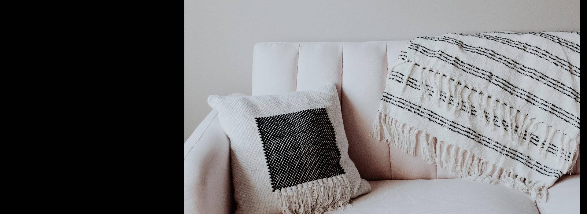 Cream colored couch with a throw pillow and blanket.