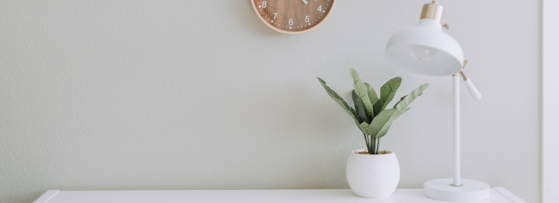 white desk with clock, plant and lamp  on desk