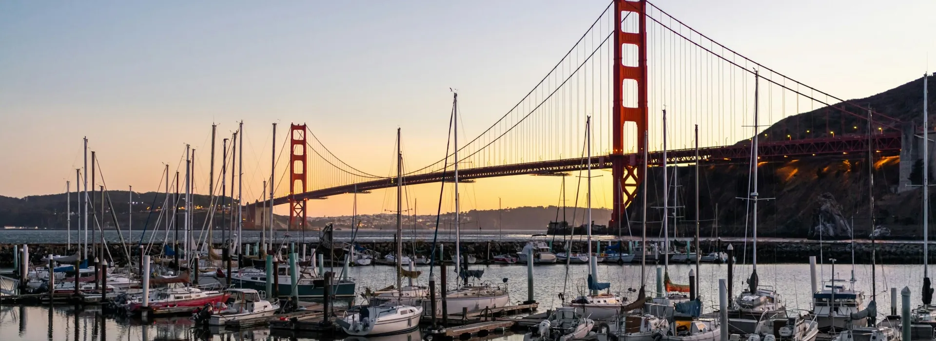 marina in sausalito viewing into SF with golden gate bridge in background and sunset past the bridge