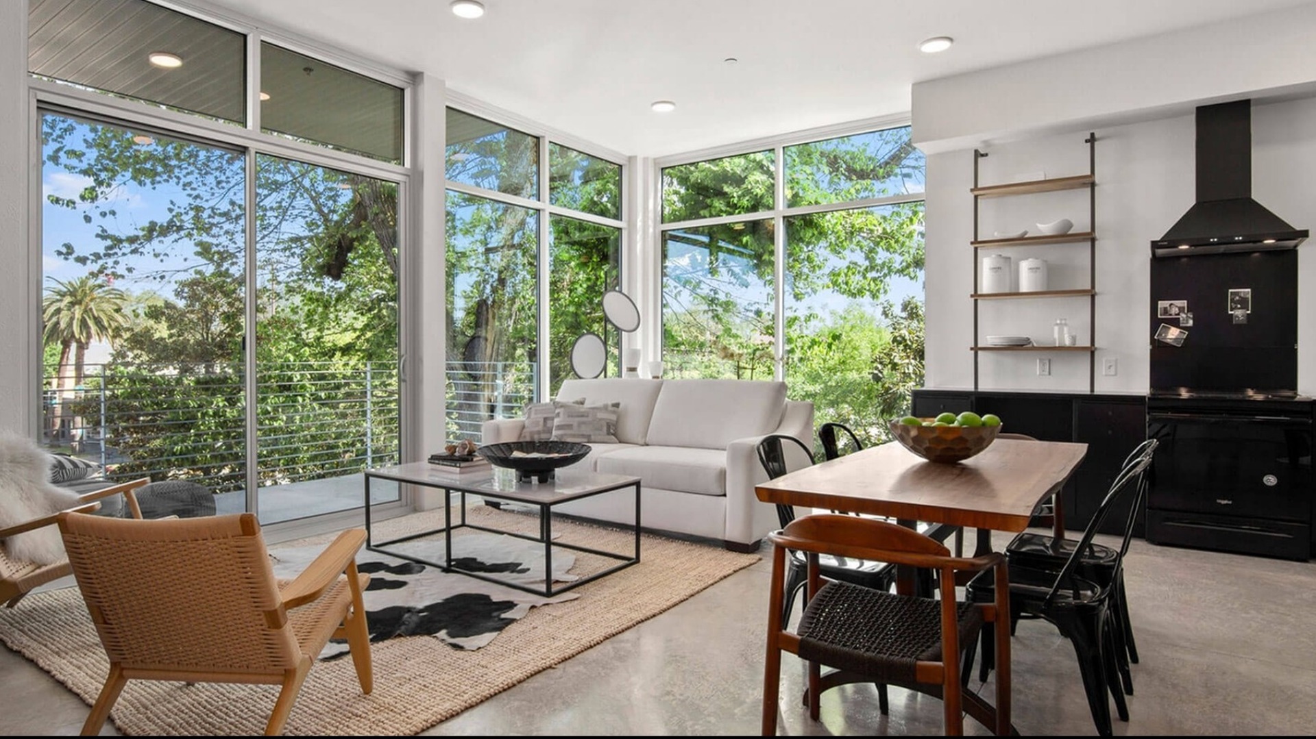 A white couch in a living room with dining area, black kitchen cabinetry, and large windows