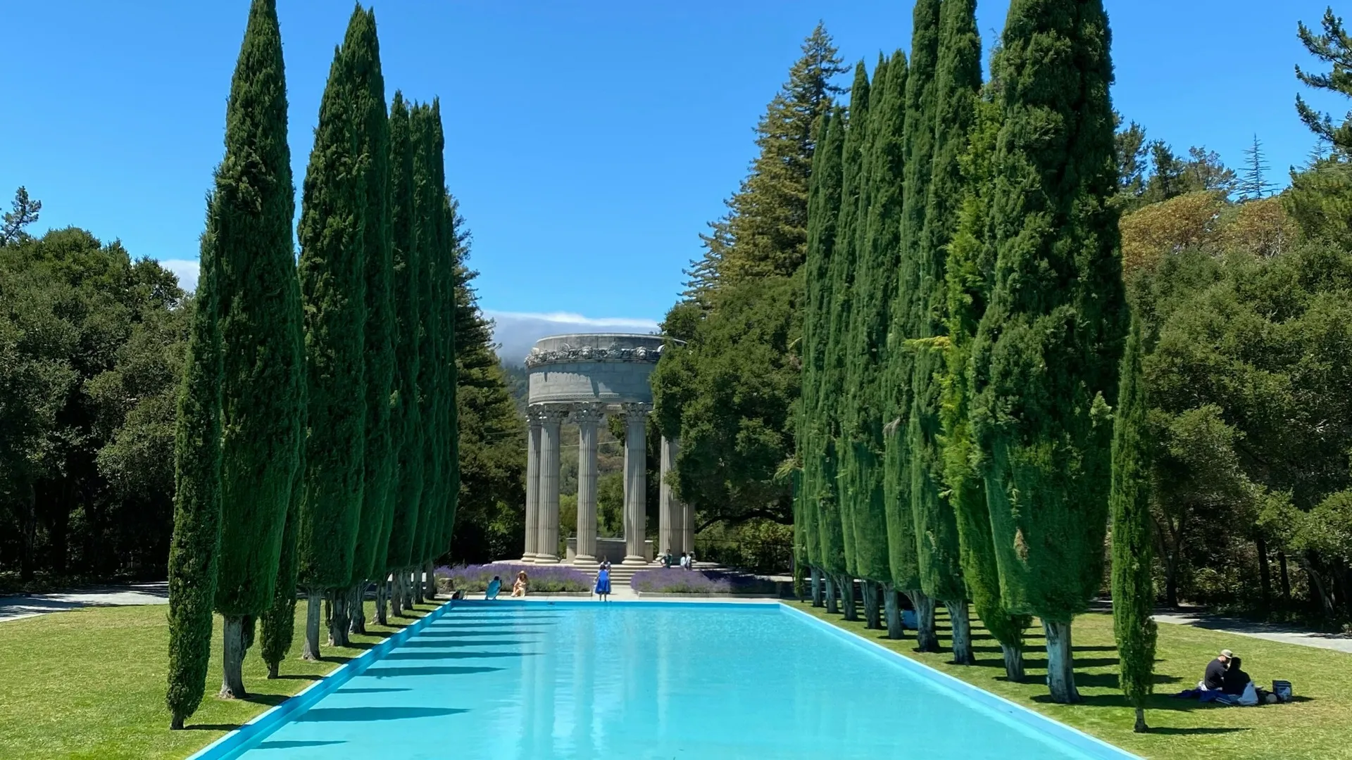 pool with greek architecture in back ground. Green trees near swimming pool.