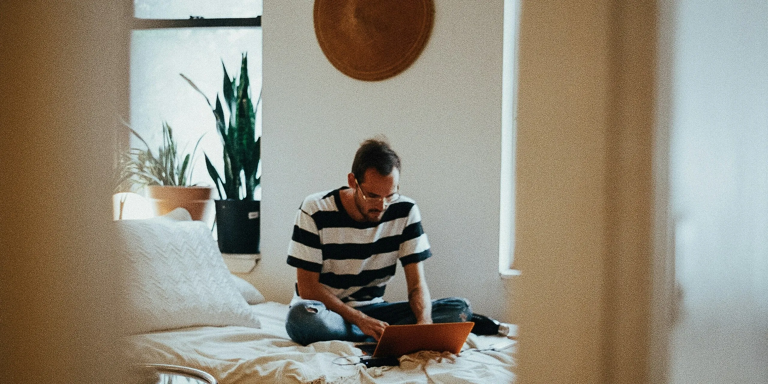 A man sitting on a bed working on a laptop