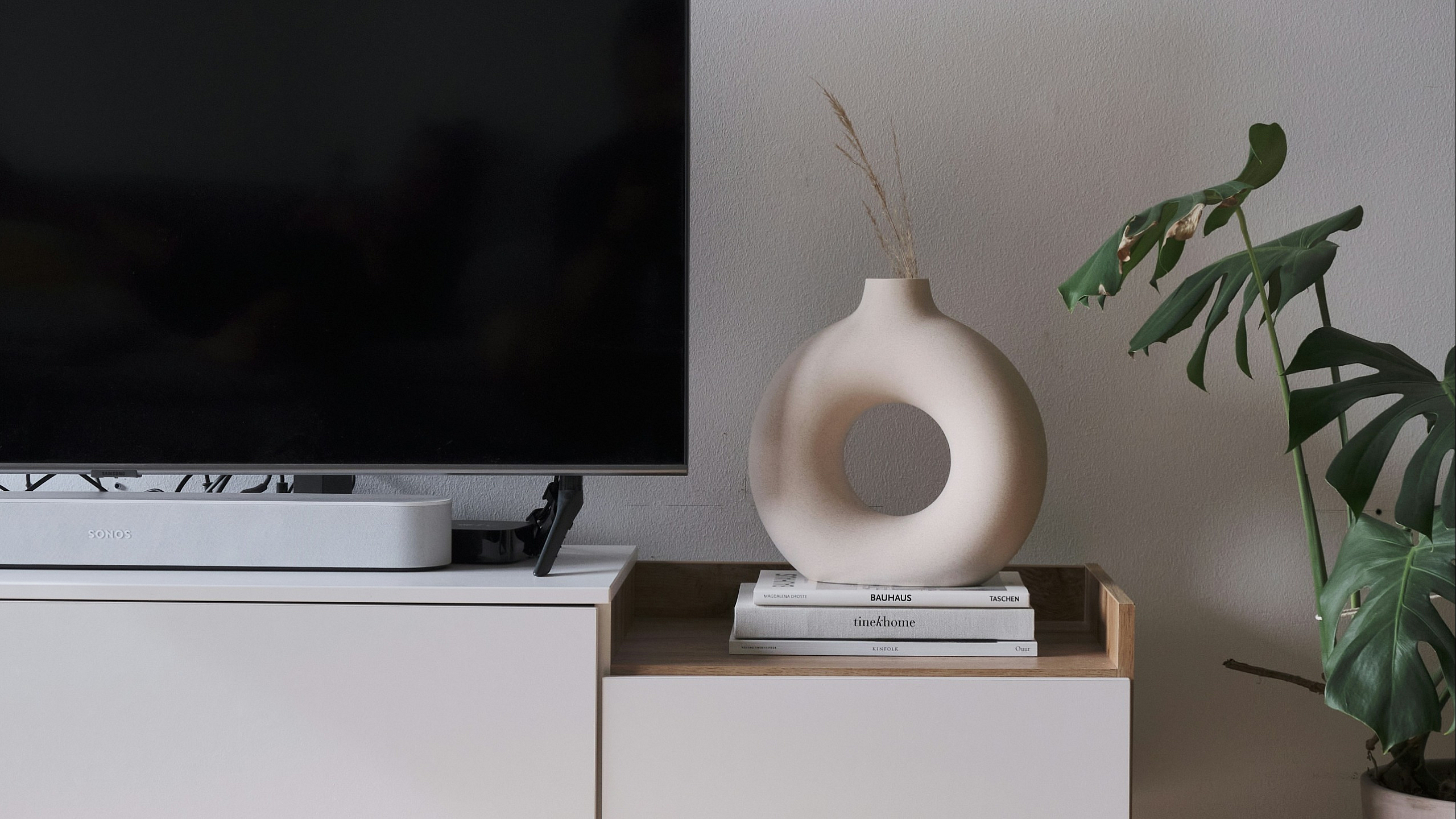 A livingroom console featuring a TV, coffee table books, and white clay vase
