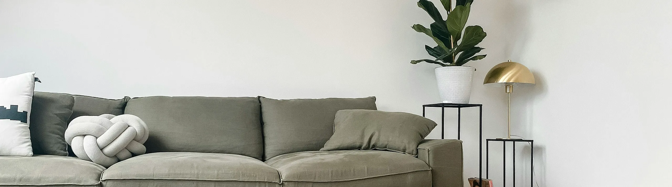 A couch in a livingroom next to a small plant and gold toned lamp