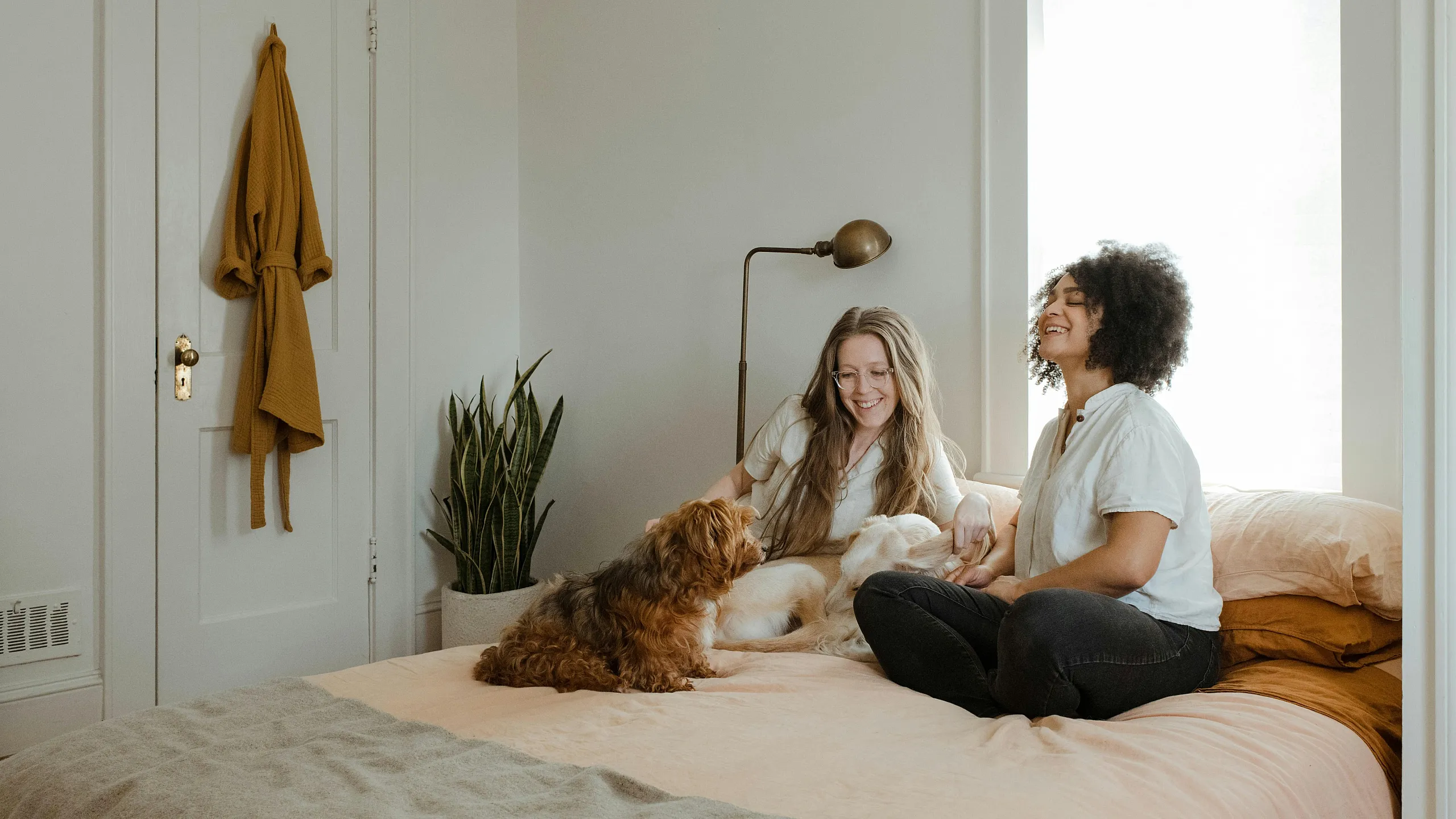 Two women and a dog sitting on a bed  smiling