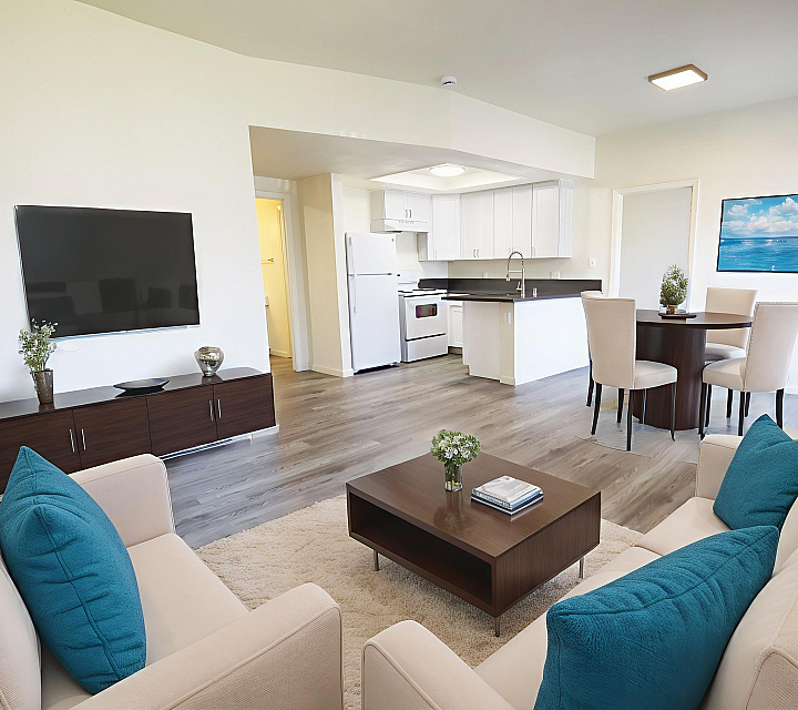 Staged living room with hard surface flooring and view of kitchen with white cabinets
