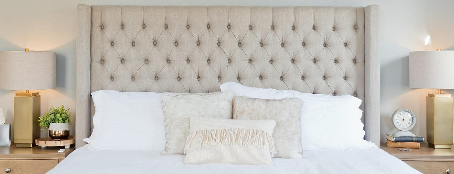 Picture of a bed with white sheets, cream headboard and two gold bedside lamps