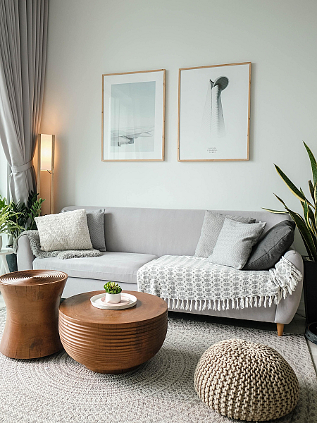 A grey couch in a bright livingoom with throw pillows, side tables and two art posters on the wall