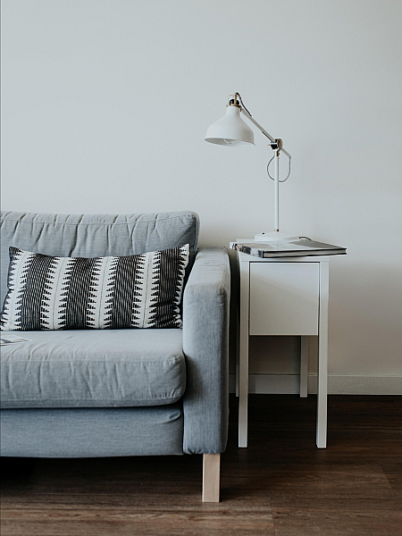Grey couch with a black and white throw pillow, a smal white lamp on top of a mini side table