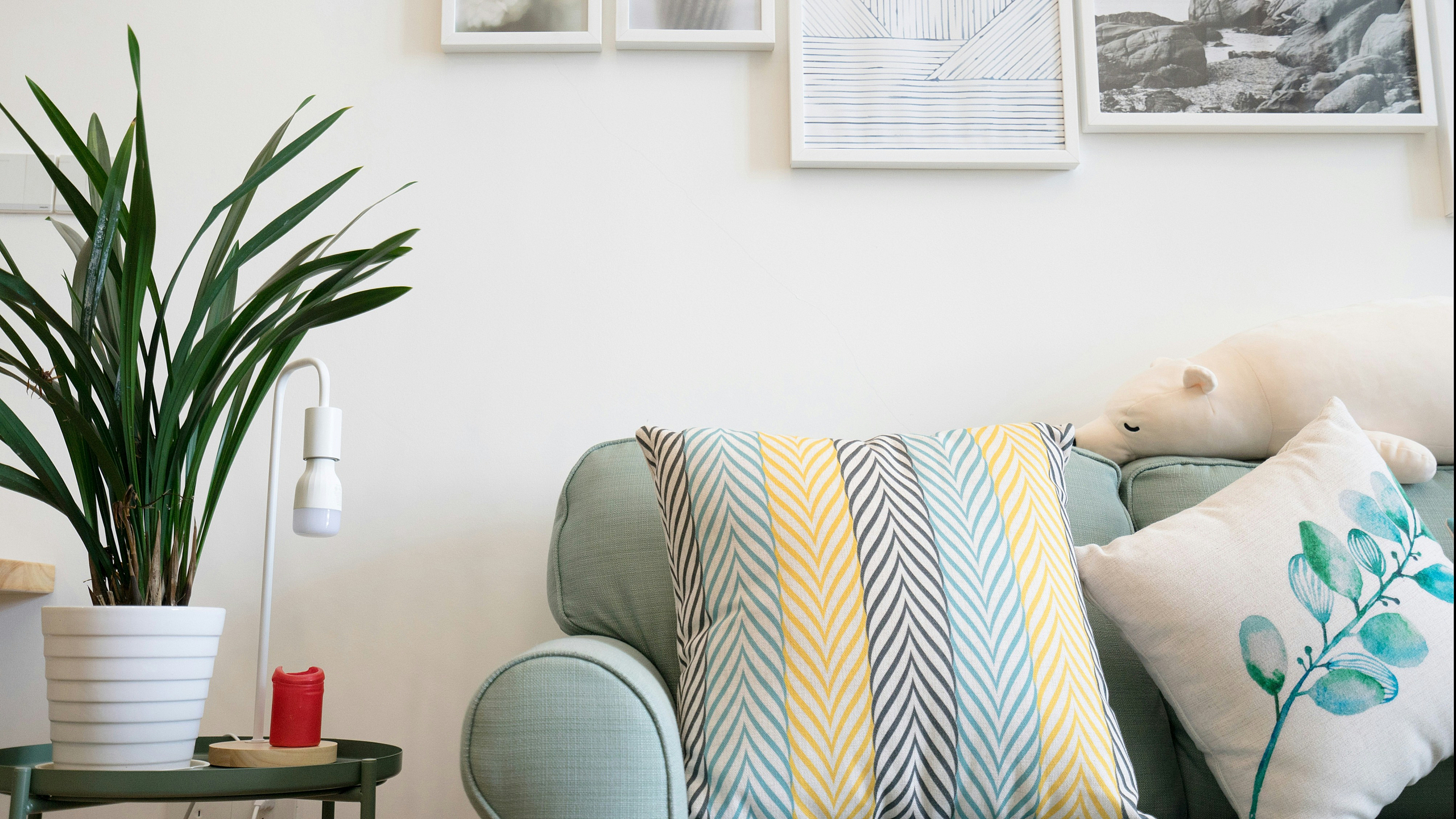 A cozy living space with a light blue sofa adorned with striped and leaf-patterned cushions. A white pot plant and minimalist wall art add a modern touch.