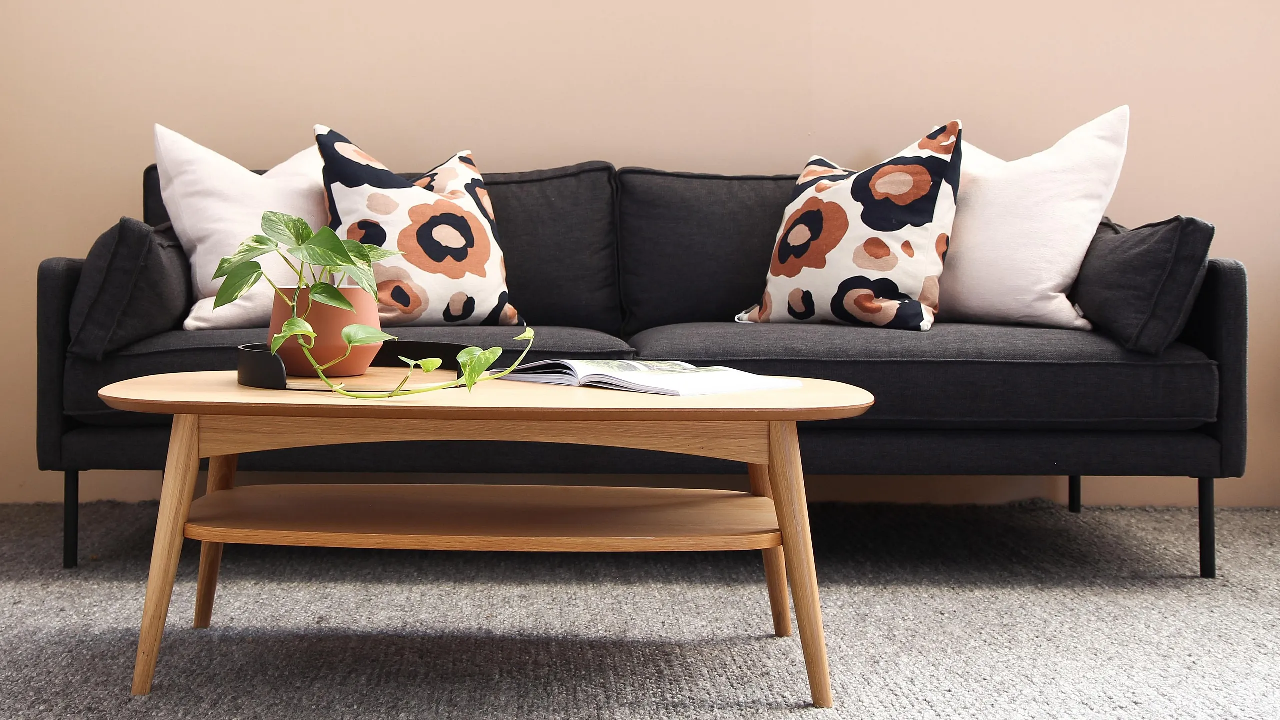 Darck grey couch with two throw pillows and a small plant on a light wood coffee table