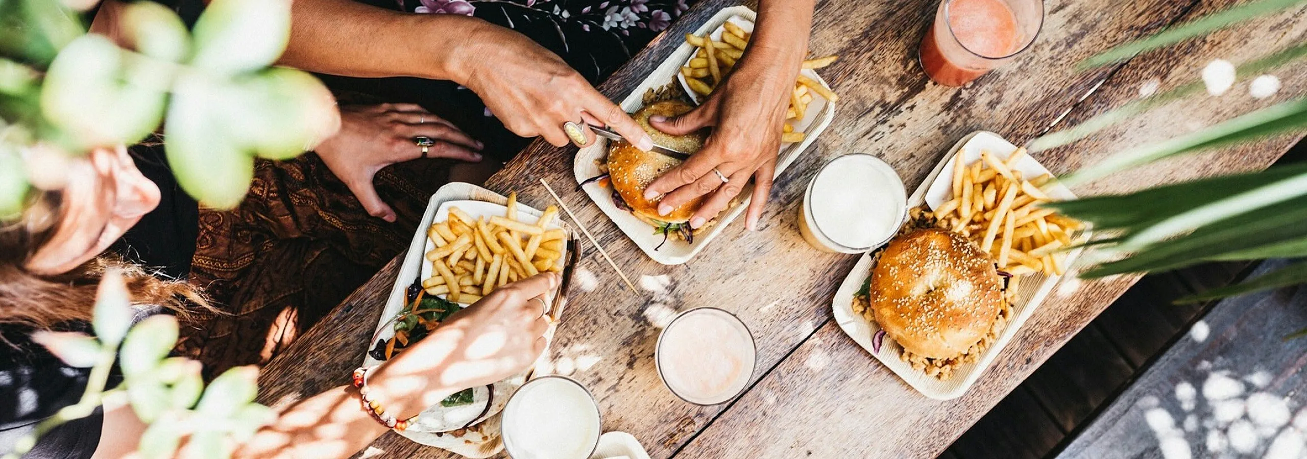 friends gathered around a brightly lit wooden table, enjoying burgers and french fries