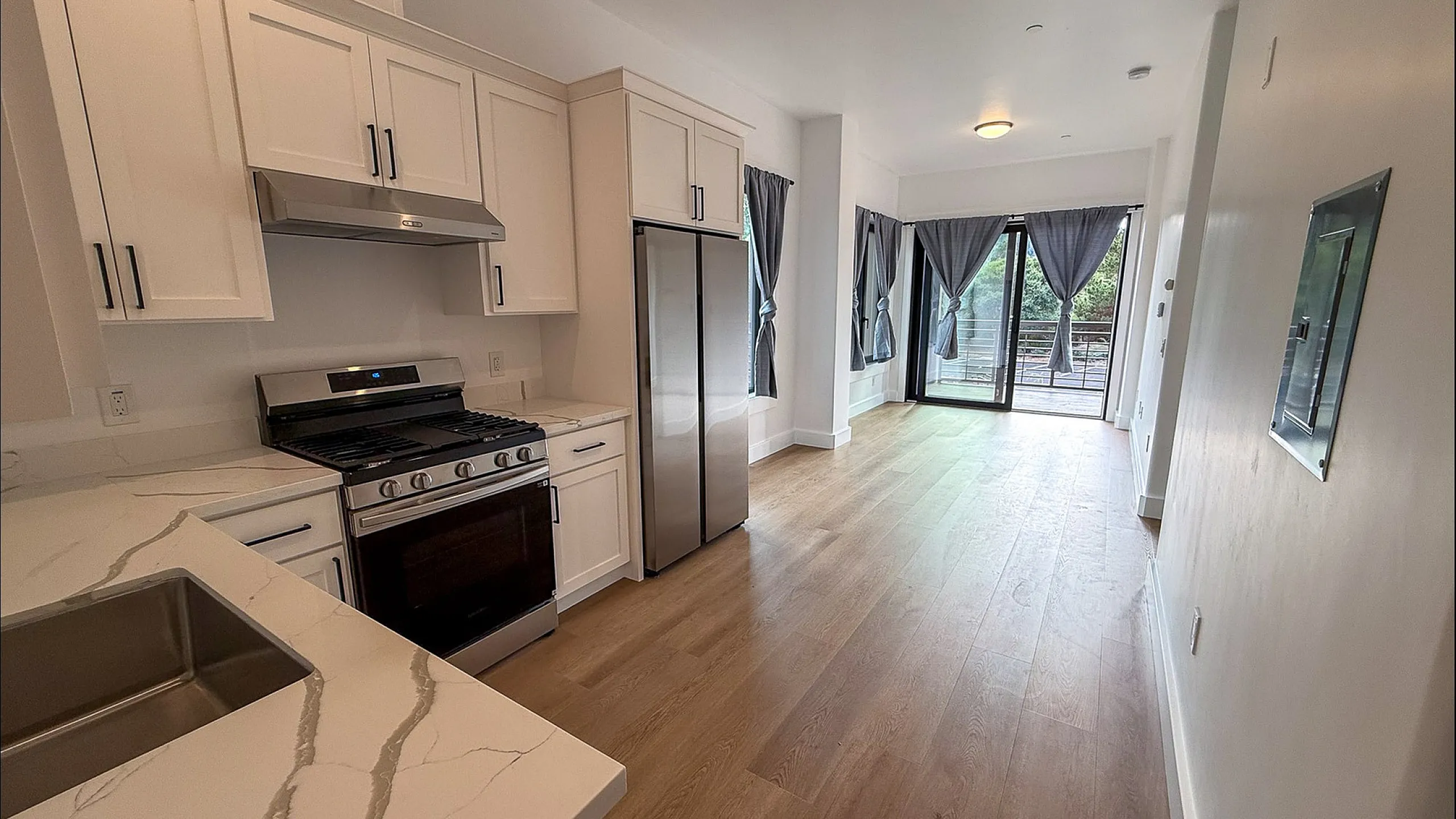Kitchen with granite counters, white cabinets, and stainless steel appliances looking towards living room with large windows