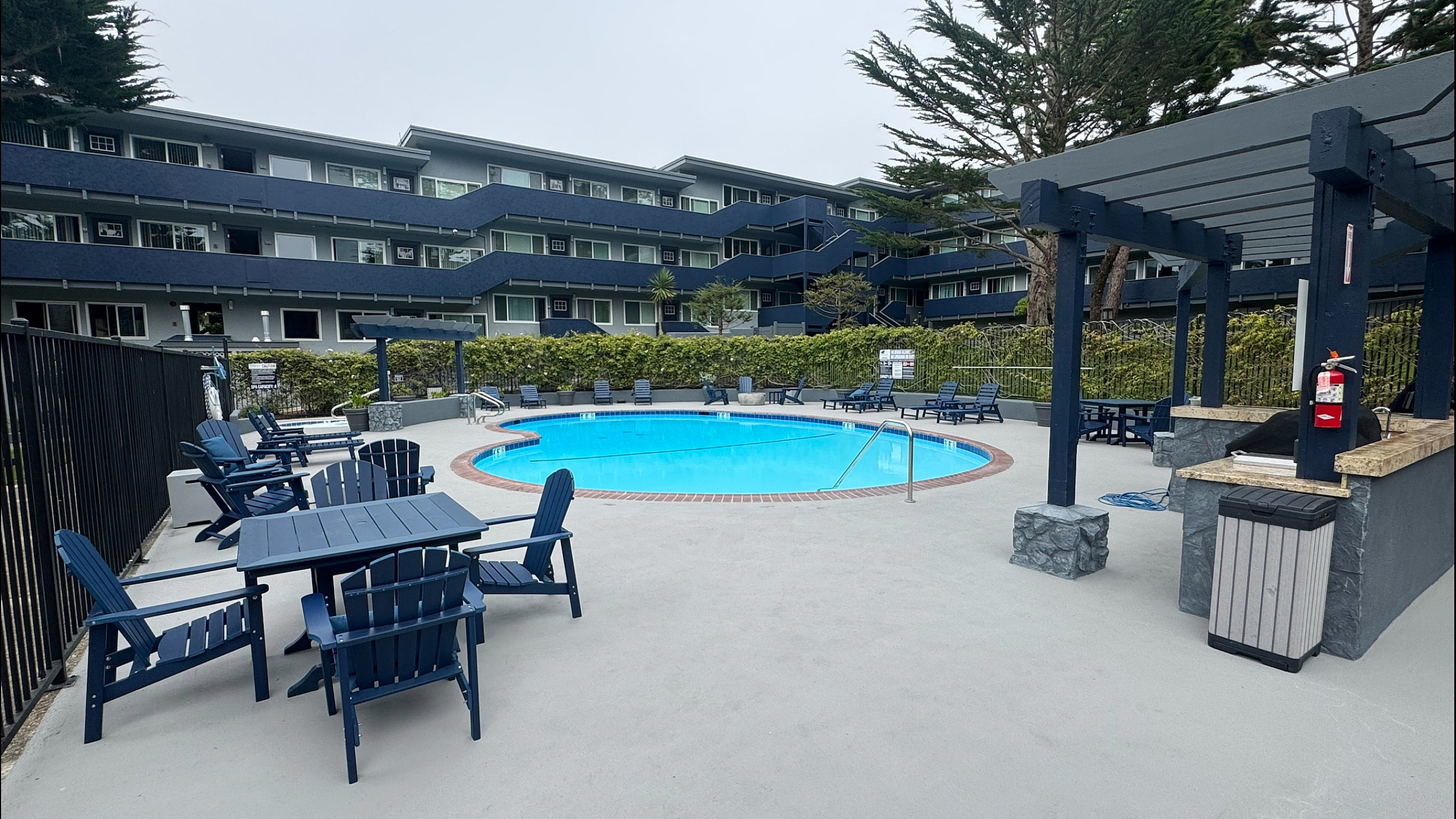 An exterior view of a swimming pool area, lounge chairs, and a multi-story apartment complex.
