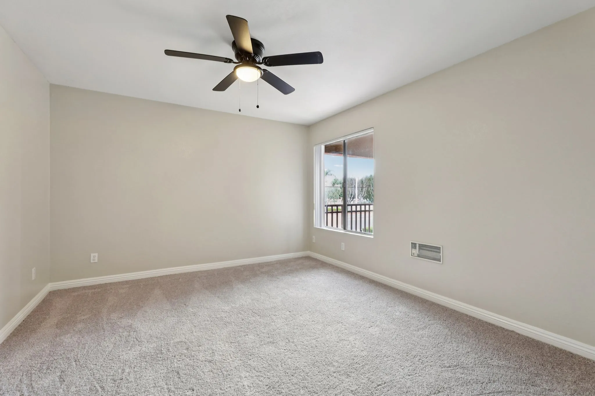 Bright and spacious room with plush carpet, ceiling fan, and large window offering a scenic view.
