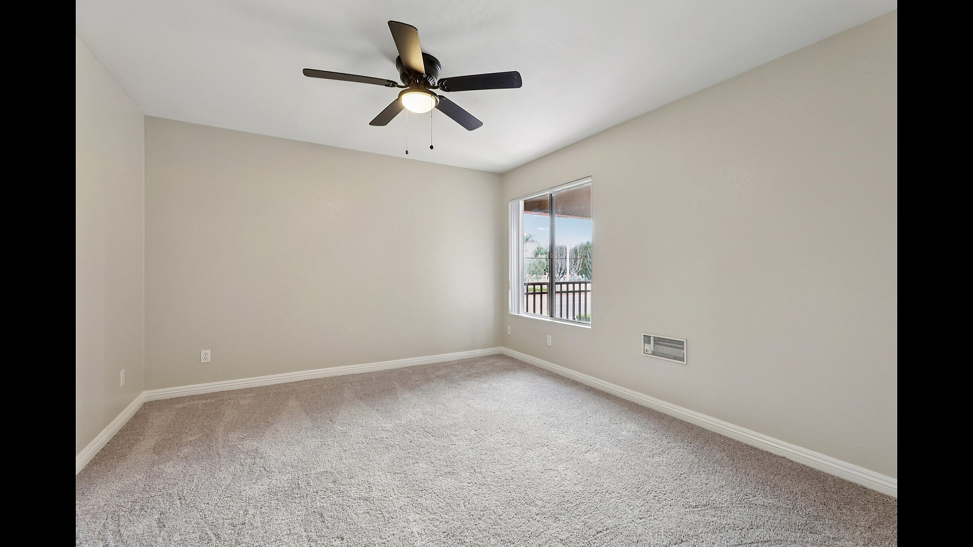 Bright and airy bedroom with plush carpeting, modern ceiling fan, and large window showcasing a scenic view.