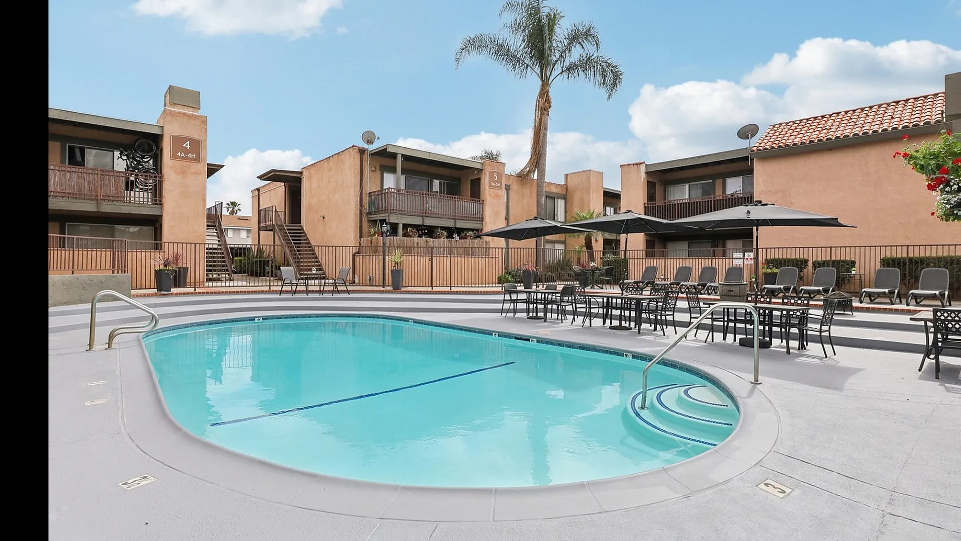 Inviting apartment complex with a sparkling outdoor pool, relaxing lounge area, and lush palm tree backdrop.