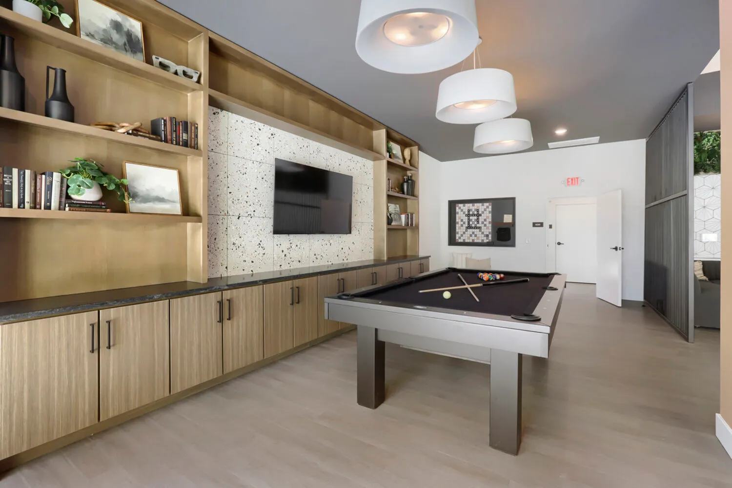 Garrett Uptown clubhouse billiards and game room with pool table, terrazzo TV wall, brass built-in shelving, and board games in Chandler, AZ