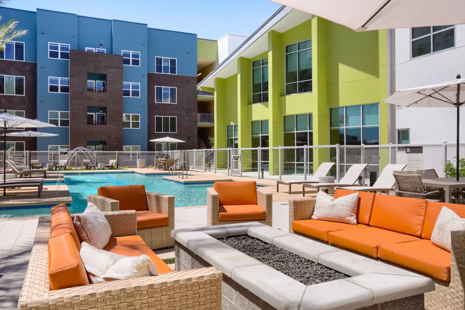 Cozy outdoor patio with bright orange furniture surrounding a gas fire pit, next to the pool.