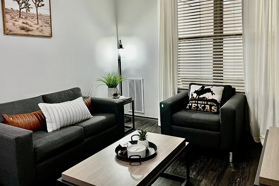 Cozy living room with modern gray sofas, a stylish coffee table, and natural light streaming through large windows, perfect for relaxing.