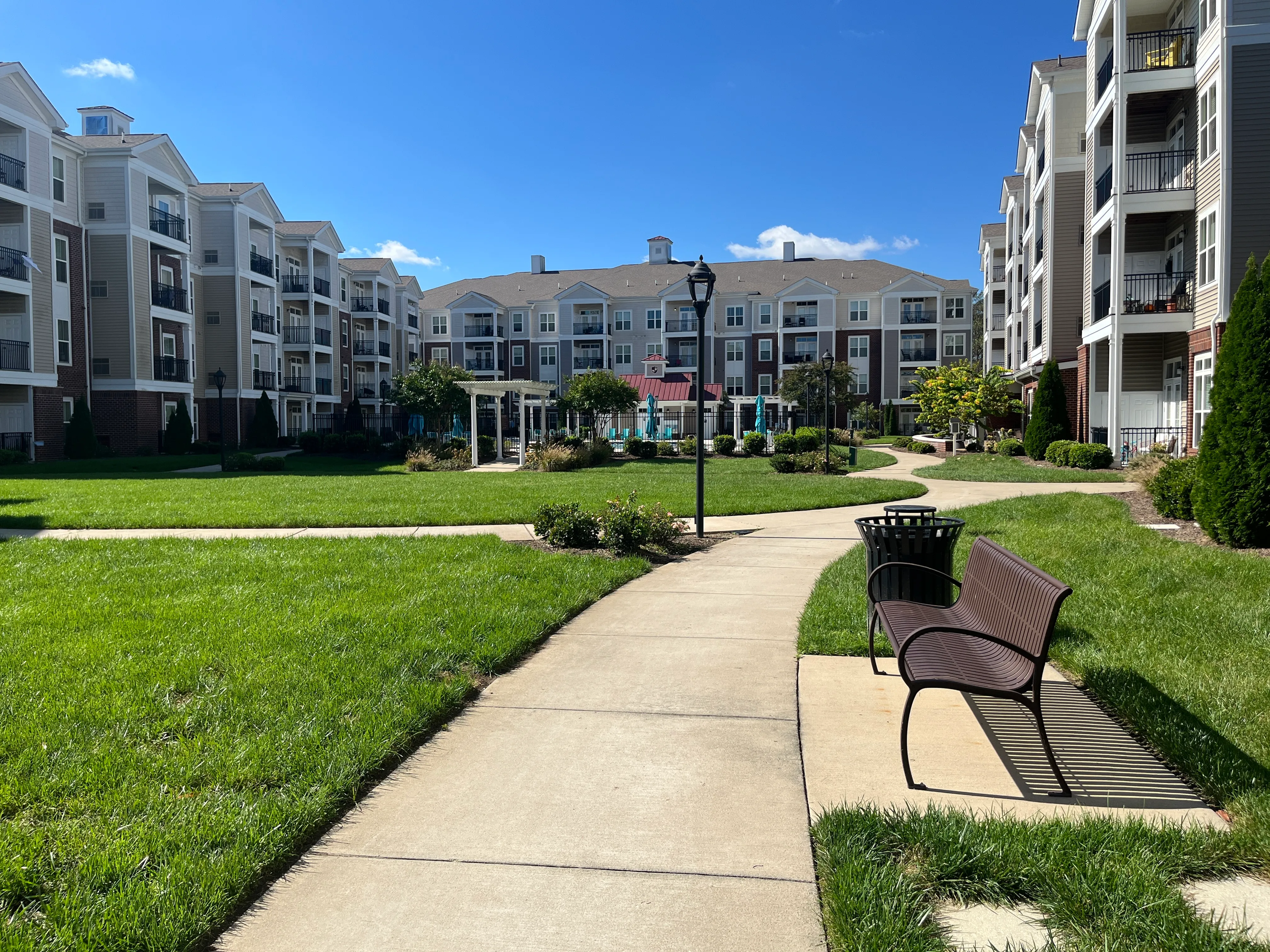 Charming apartment complex with well-manicured lawns, inviting walking paths, and beautiful architectural design under a bright blue sky.