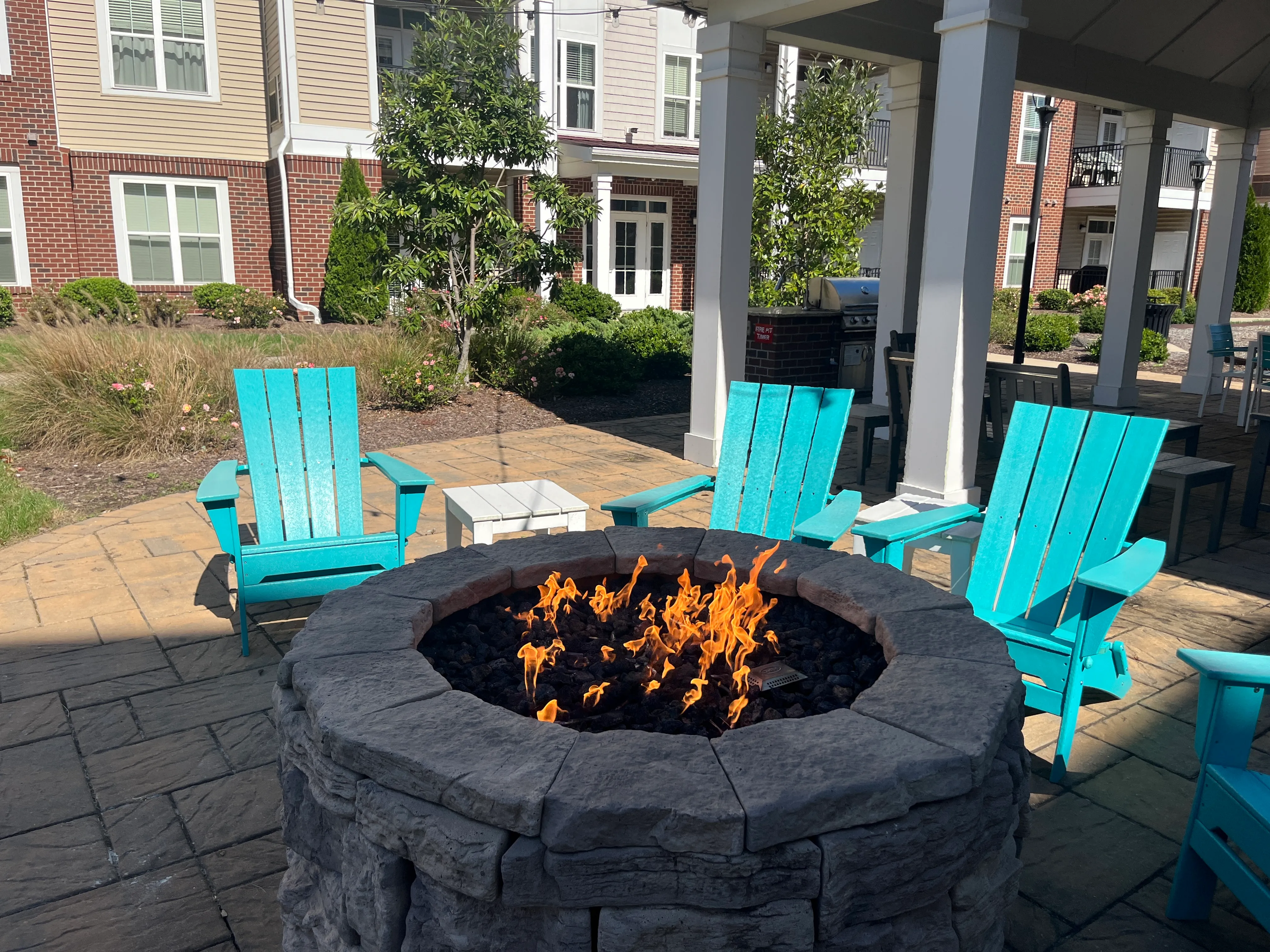Charming outdoor patio with vibrant turquoise chairs surrounding a cozy stone fire pit, perfect for relaxing evenings.