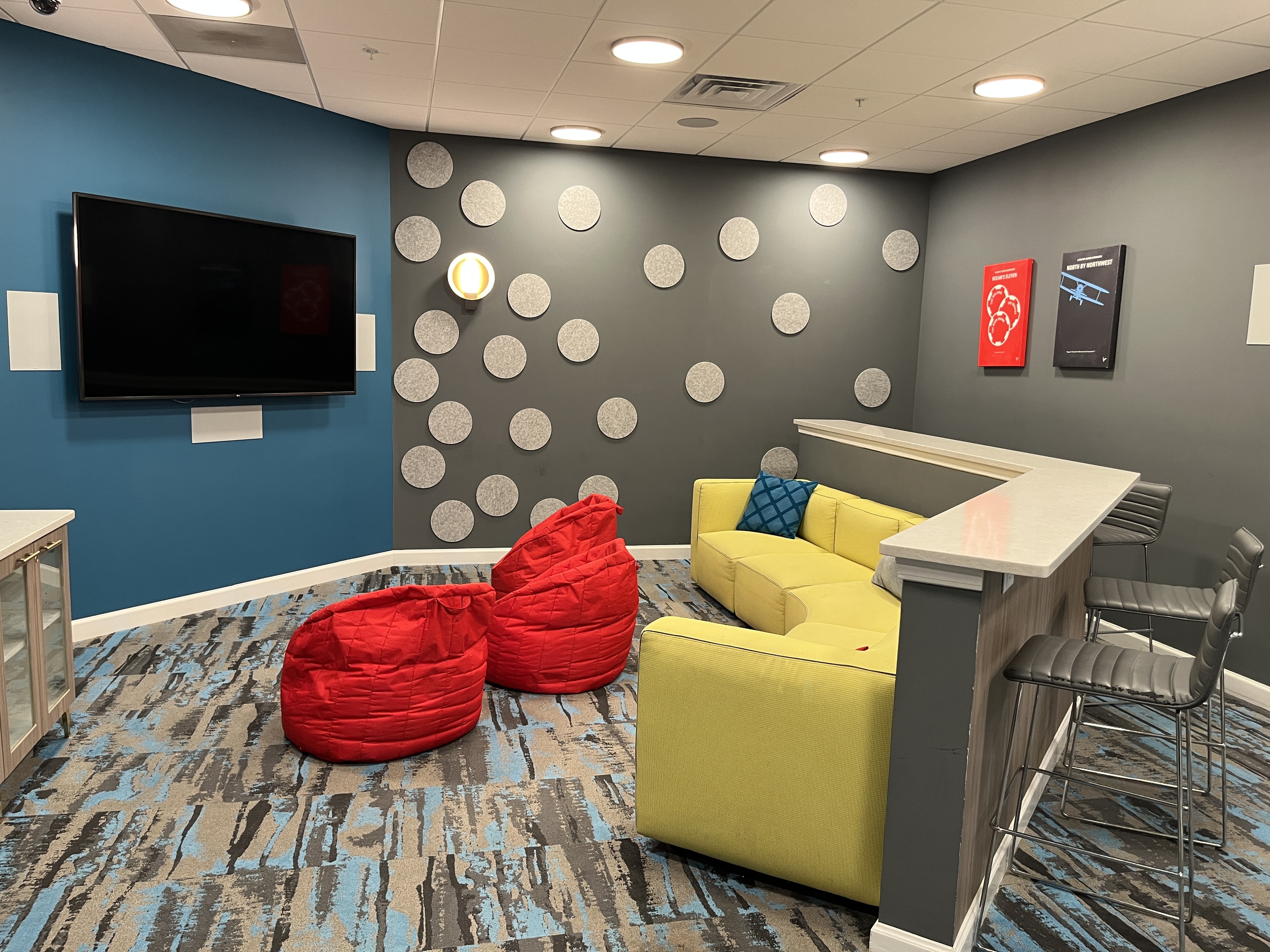 Bright, modern lounge area featuring a vibrant yellow sofa, red bean bags, and a large flat-screen TV, ideal for relaxation and entertainment.