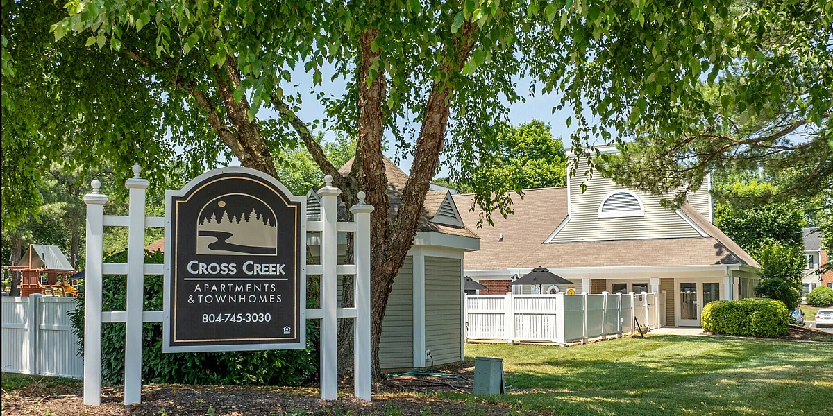 Charming entrance to Cross Creek Apartments and Townhomes with lush greenery and modern signage.