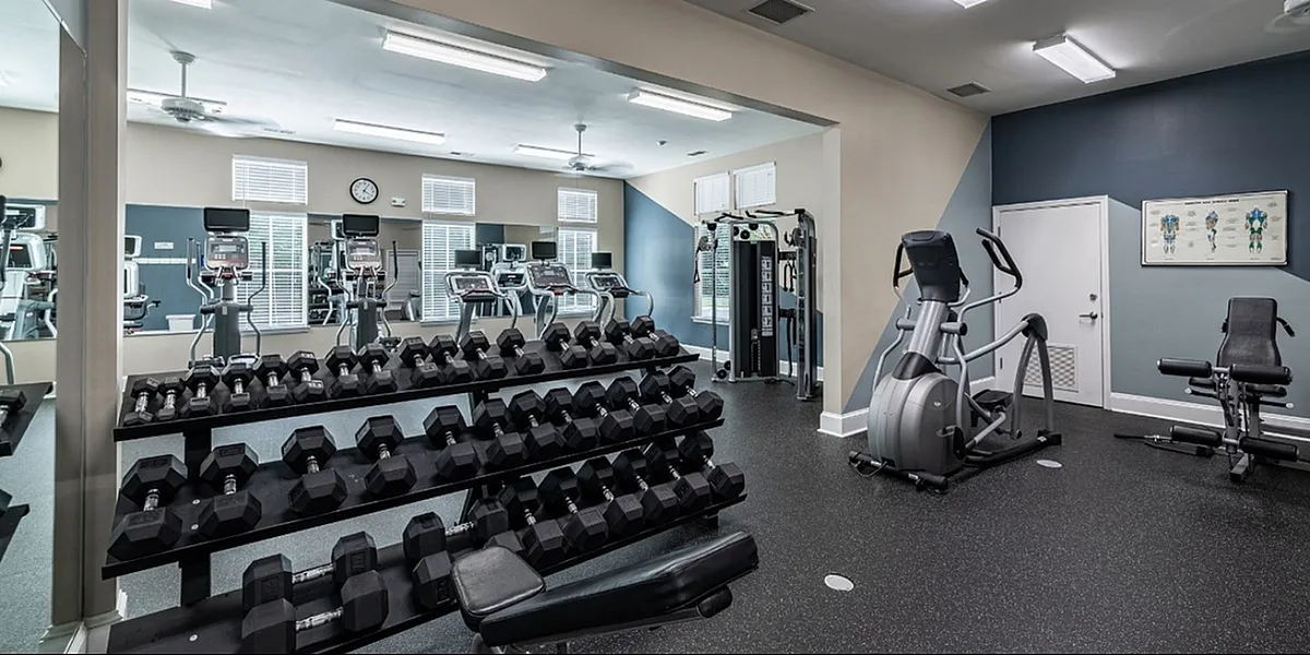Bright, fully equipped fitness room with treadmills, ellipticals, and mirrored wall.