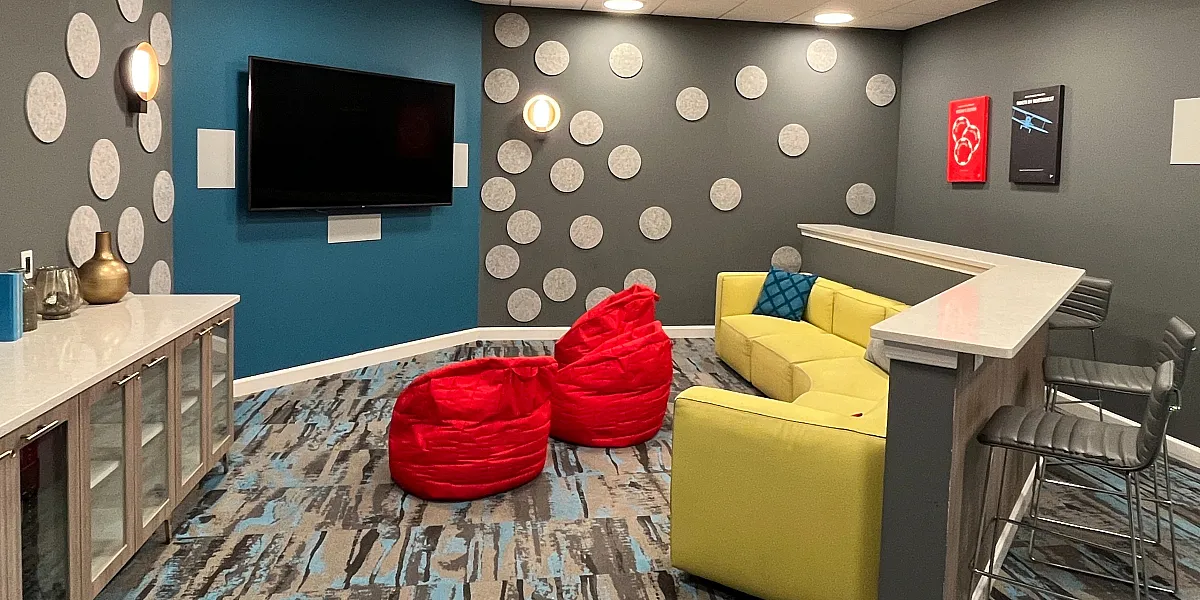 Vibrant lounge area with modern decor, featuring a yellow sofa, red bean bags, and a large flat-screen TV, ideal for relaxation and entertainment.