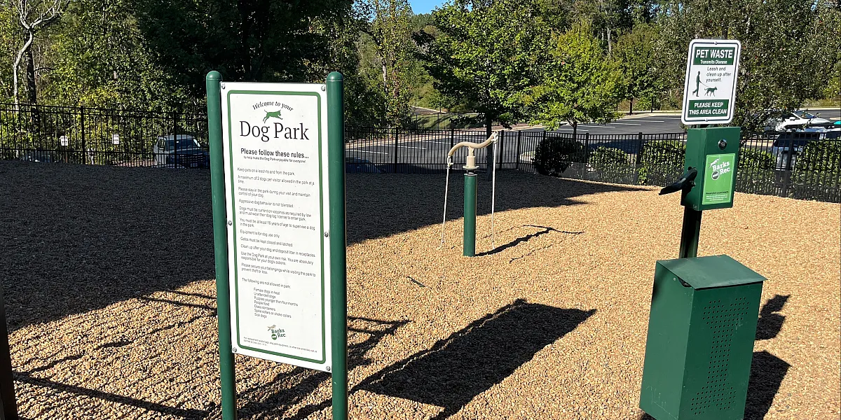 Inviting dog park with green amenities and clear signage, surrounded by lush trees, perfect for playful pets.