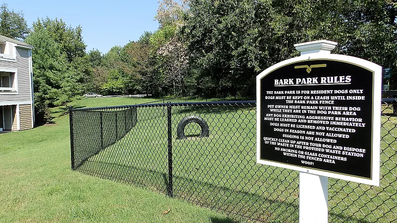 Pet-friendly apartment community showcasing a fenced bark park with vibrant greenery, modern building exterior, and clear blue skies.