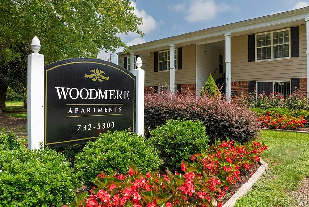 Charming Woodmere Apartments entrance surrounded by vibrant landscaping and lush greenery.