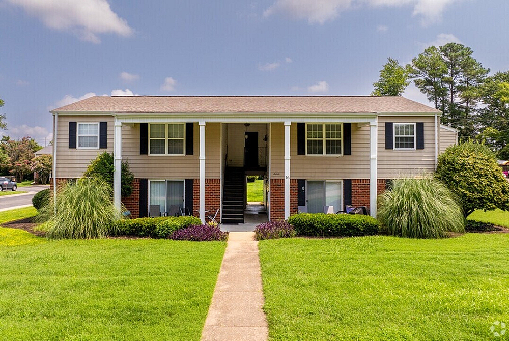 Charming duplex with classic architecture, lush green lawn, and inviting entrance under a clear blue sky.